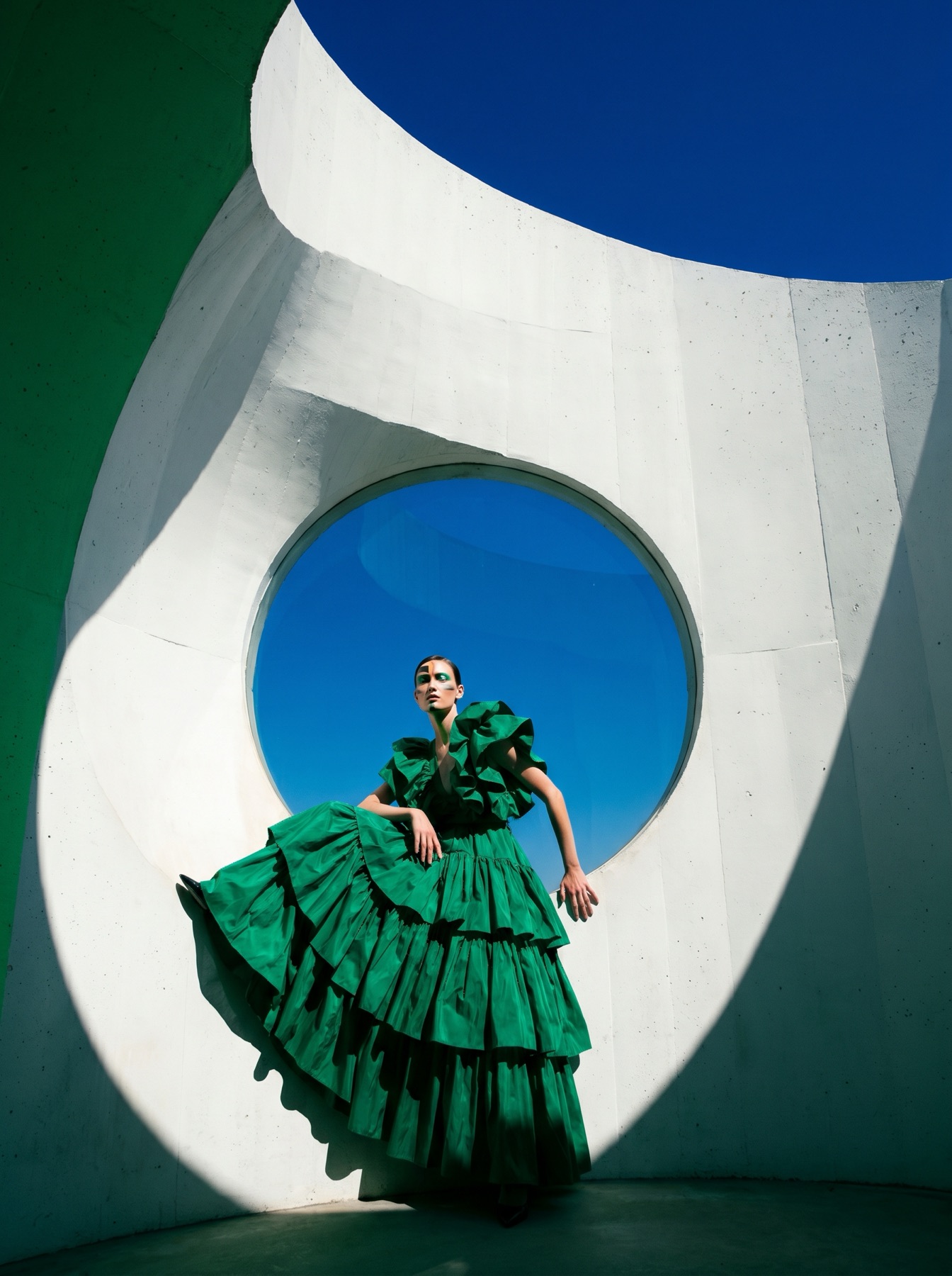 Avant-garde fashion editorial — model in emerald gown within a white sculptural form