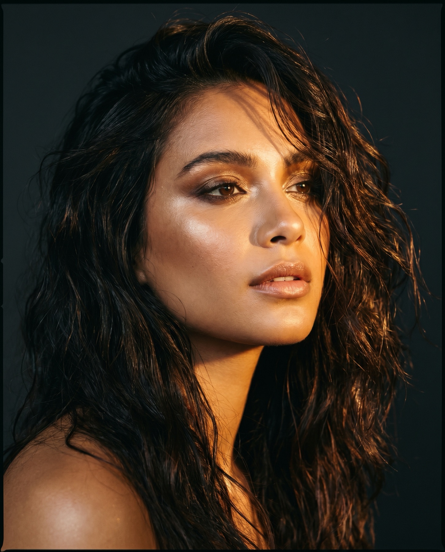 Beauty editorial portrait in warm golden light against a dark backdrop
